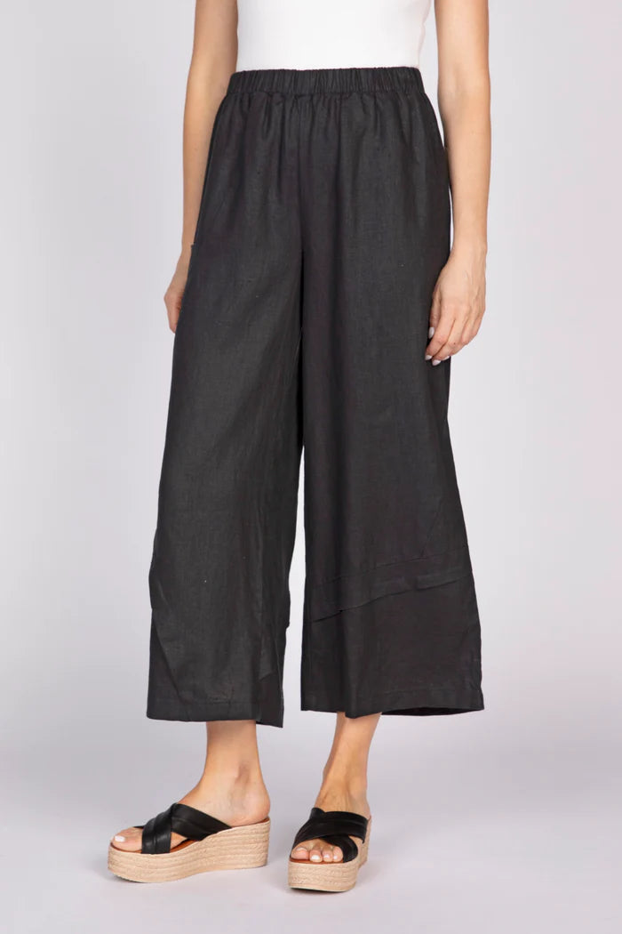 A front view of a person wearing black wide-leg linen pants with unique pleat details at the hem and black platform sandals.