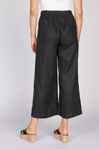 A rear view of a woman wearing black wide-leg linen pants with unique pleat details at the hem and black platform sandals.