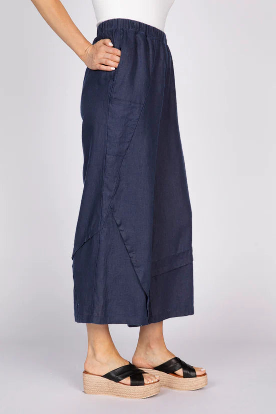 Side view of a woman wearing navy blue wide-leg linen pants with unique pleat details at the hem and black platform sandals