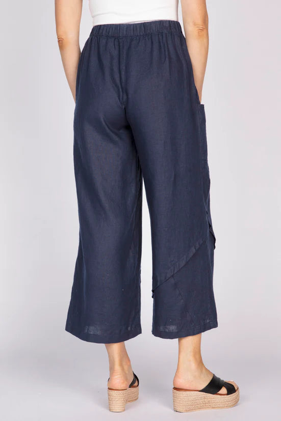 Rear view of a woman wearing navy blue wide-leg linen pants with unique pleat details at the hem and black platform sandals