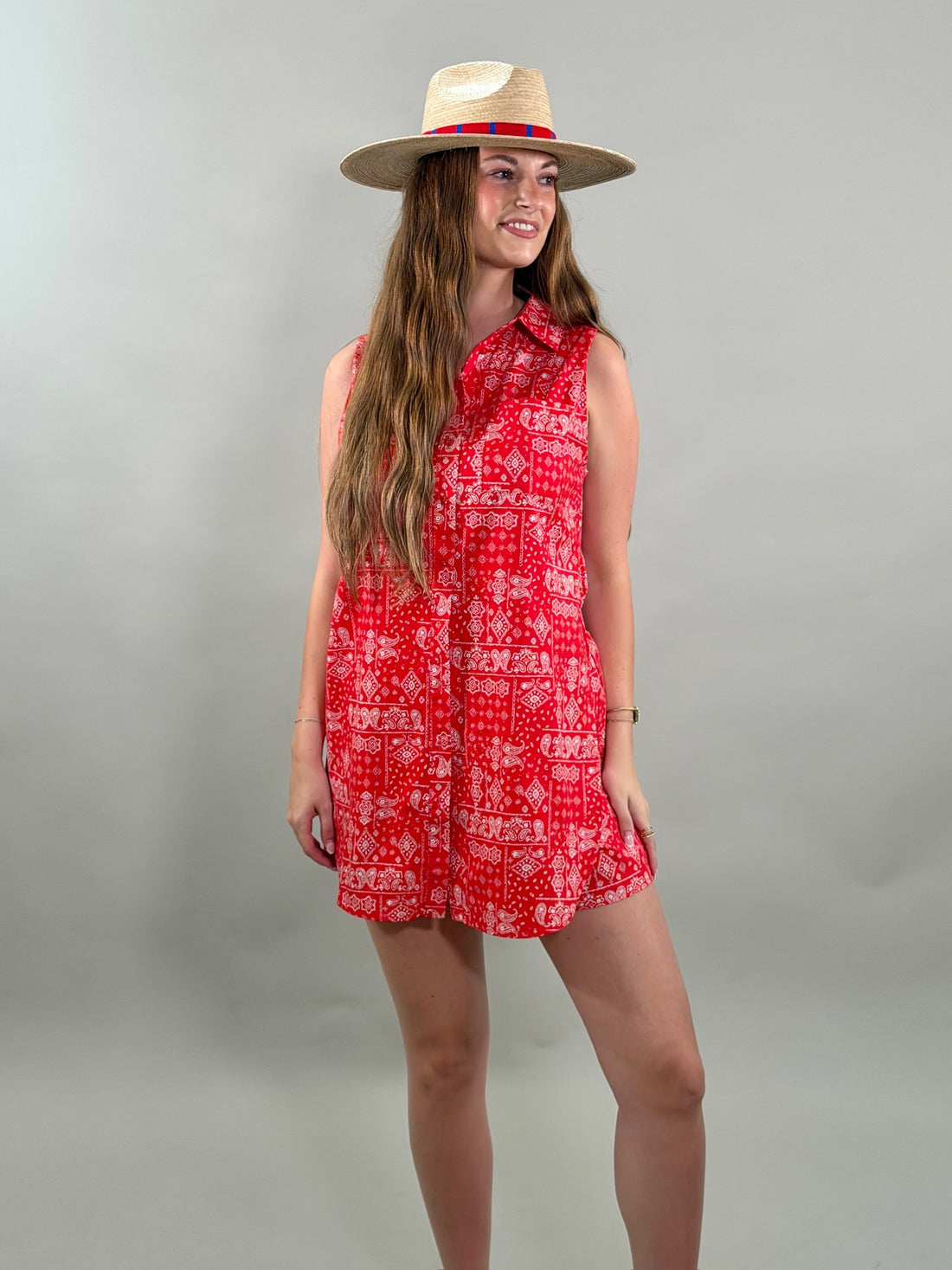 Woman wearing a red bandana patterned romper and straw hat on a gray background