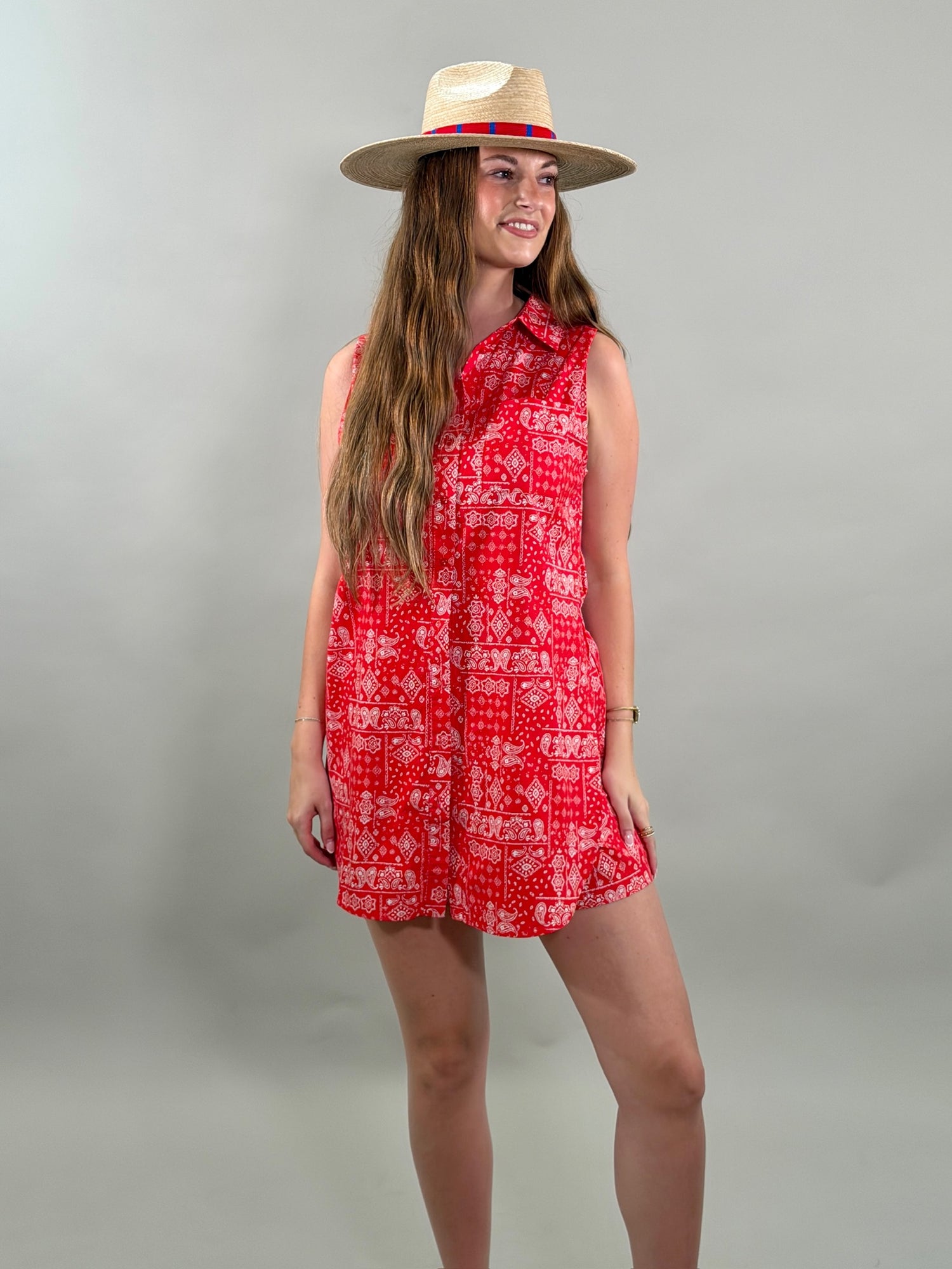 Woman wearing a red bandana patterned romper and straw hat on a gray background