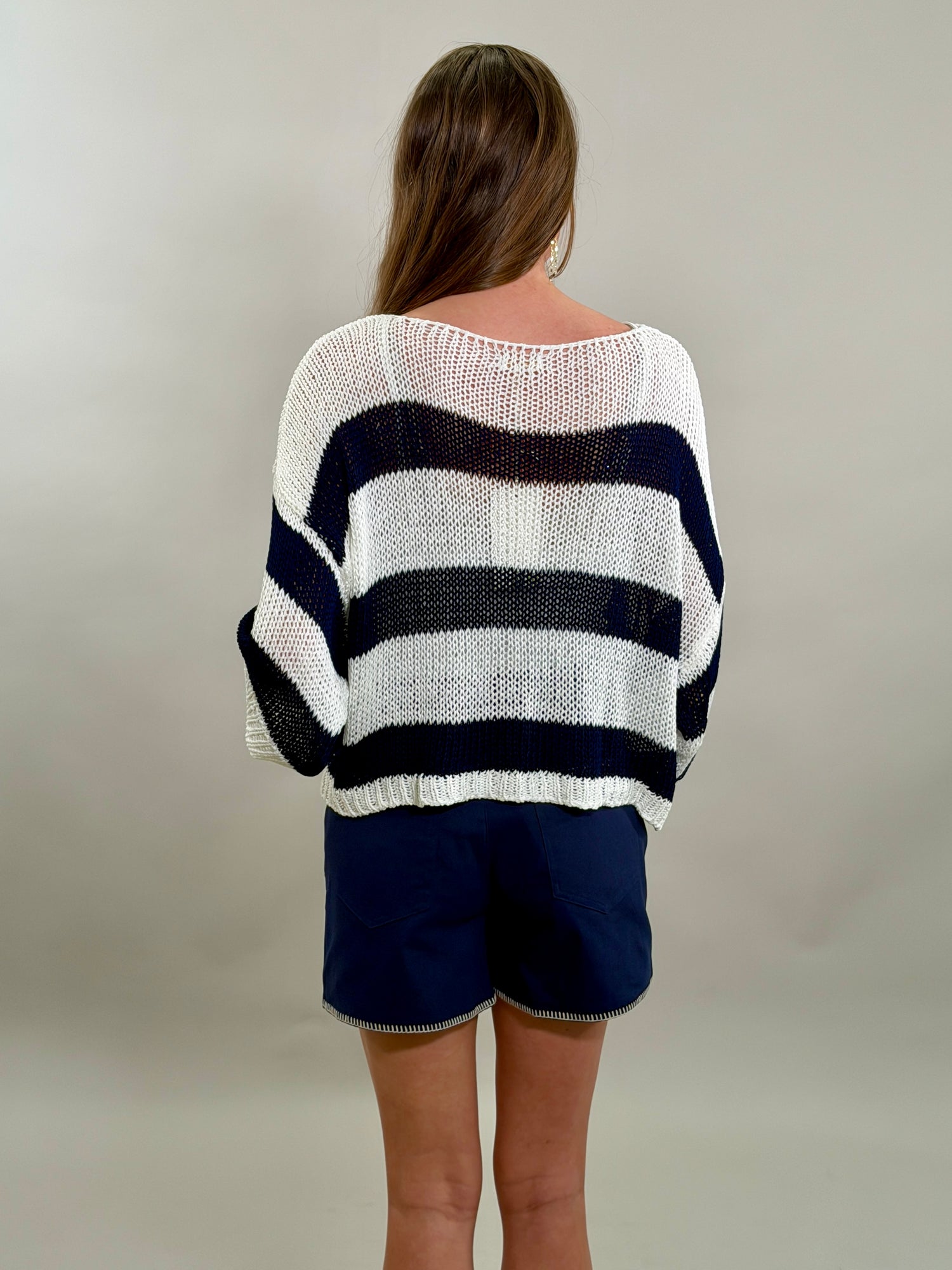 Rear view of a woman wearing a navy and white striped sweater and blue shorts against a plain background