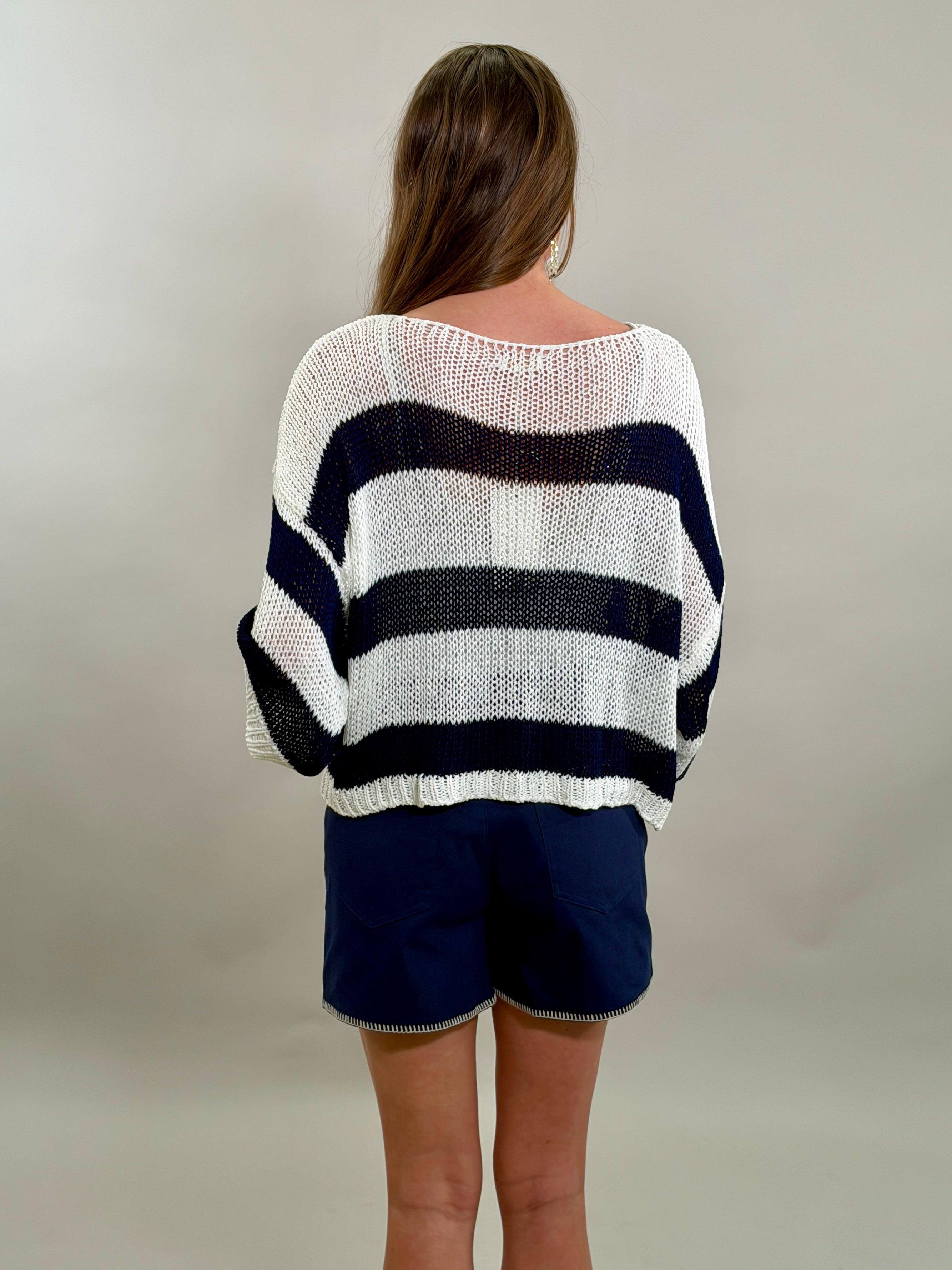 Rear view of a woman wearing a navy and white striped sweater and blue shorts against a plain background