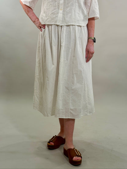 Close-up of a woman wearing a white geometric eyelet midi skirt paired with brown platform slide sandals.