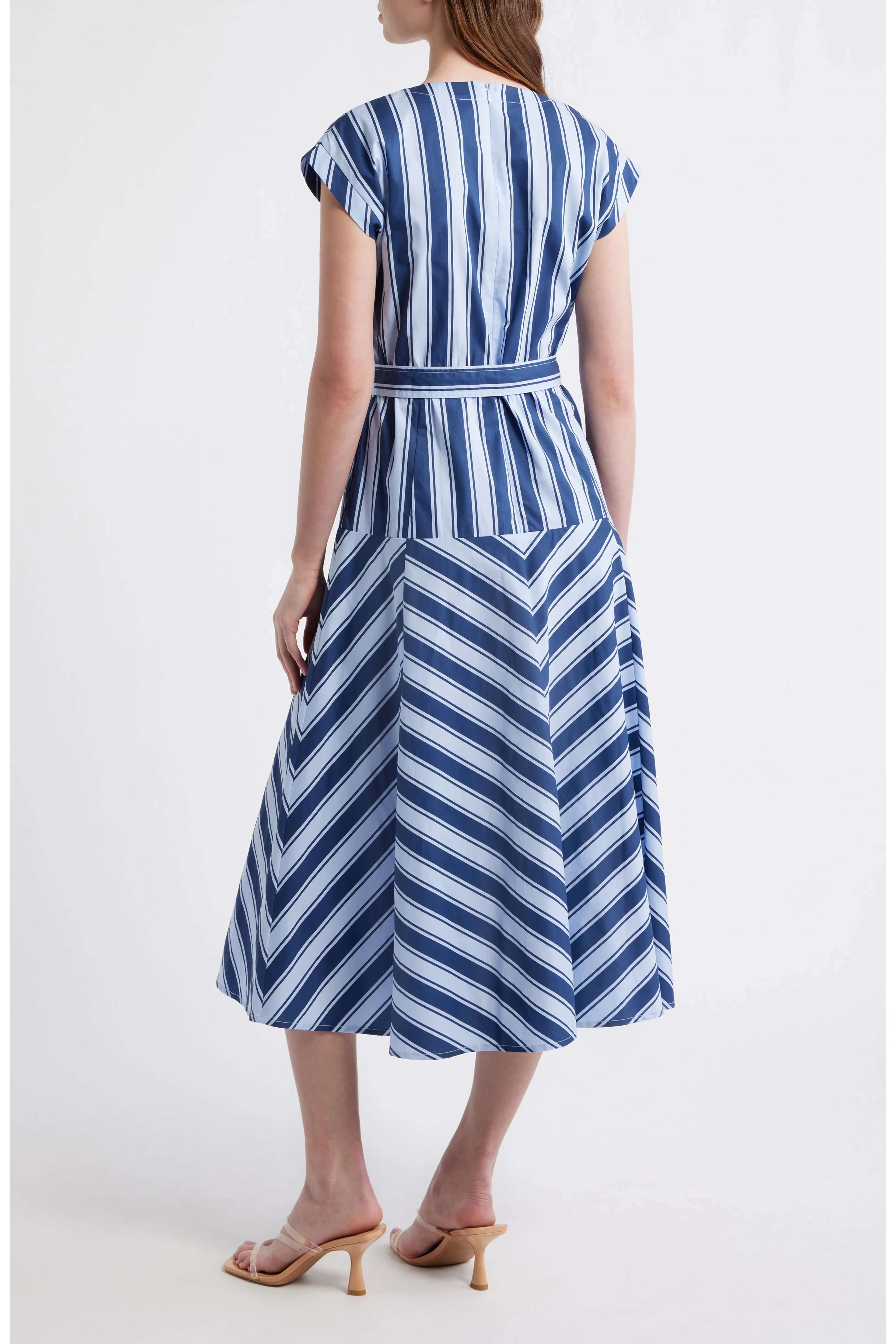 Rear view of a woman wearing a blue and white multi-directional striped midi dress with short cap sleeves and a matching fabric tie belt.