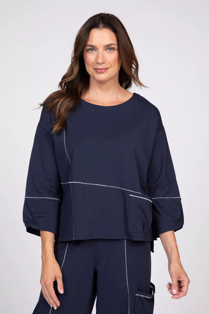 Woman wearing a navy blue three-quarter sleeve top with white contrast stitching and a front pocket.