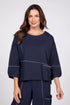 Woman wearing a navy blue three-quarter sleeve top with white contrast stitching and a front pocket.