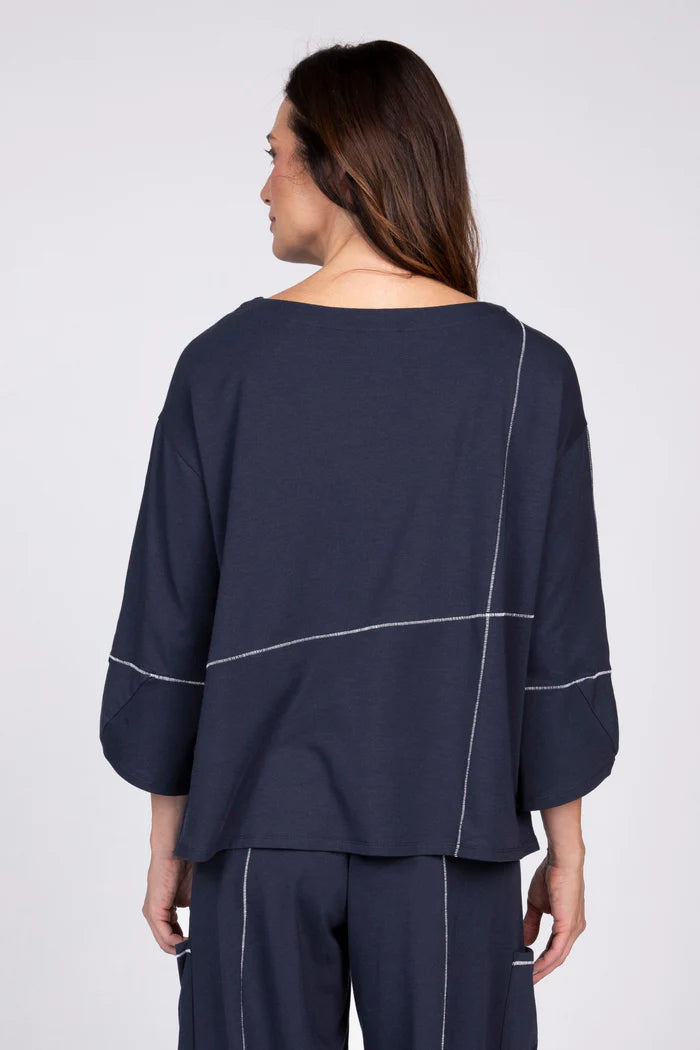 Rear view of a woman wearing a navy blue three-quarter sleeve top with white contrast stitching and a front pocket.