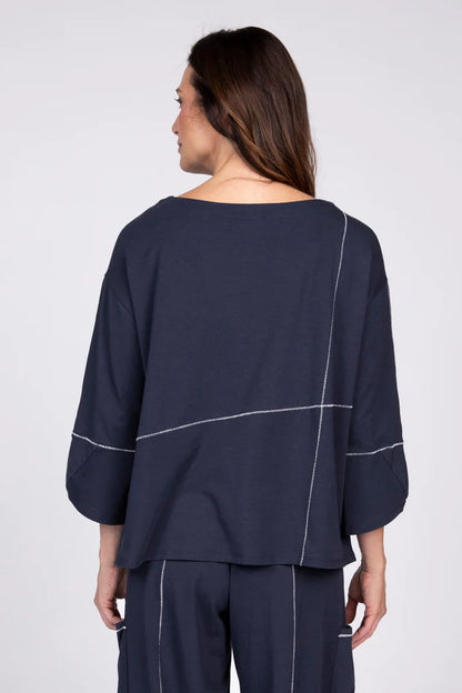 Rear view of a woman wearing a navy blue three-quarter sleeve top with white contrast stitching and a front pocket.