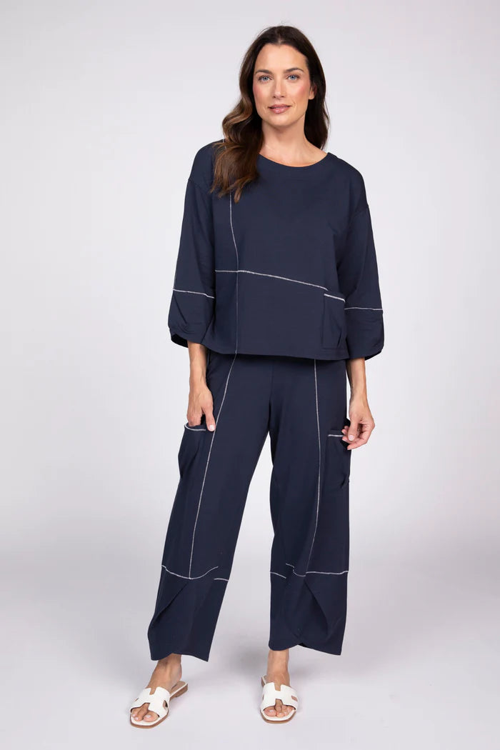 Full body view of a woman wearing a navy blue three-quarter sleeve top with white contrast stitching and a front pocket.