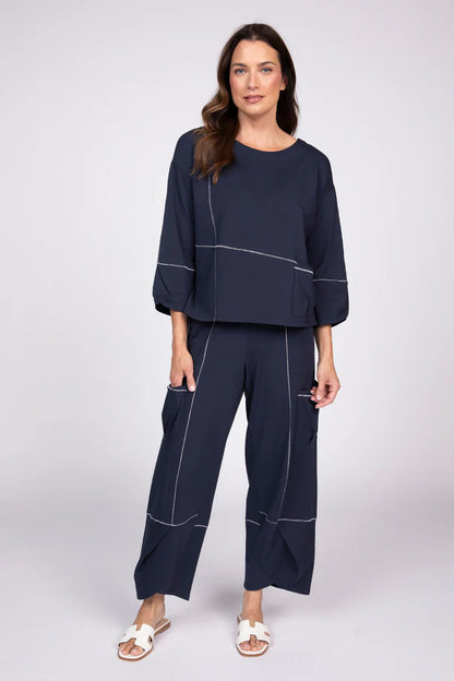 Full body view of a woman wearing a navy blue three-quarter sleeve top with white contrast stitching and a front pocket.
