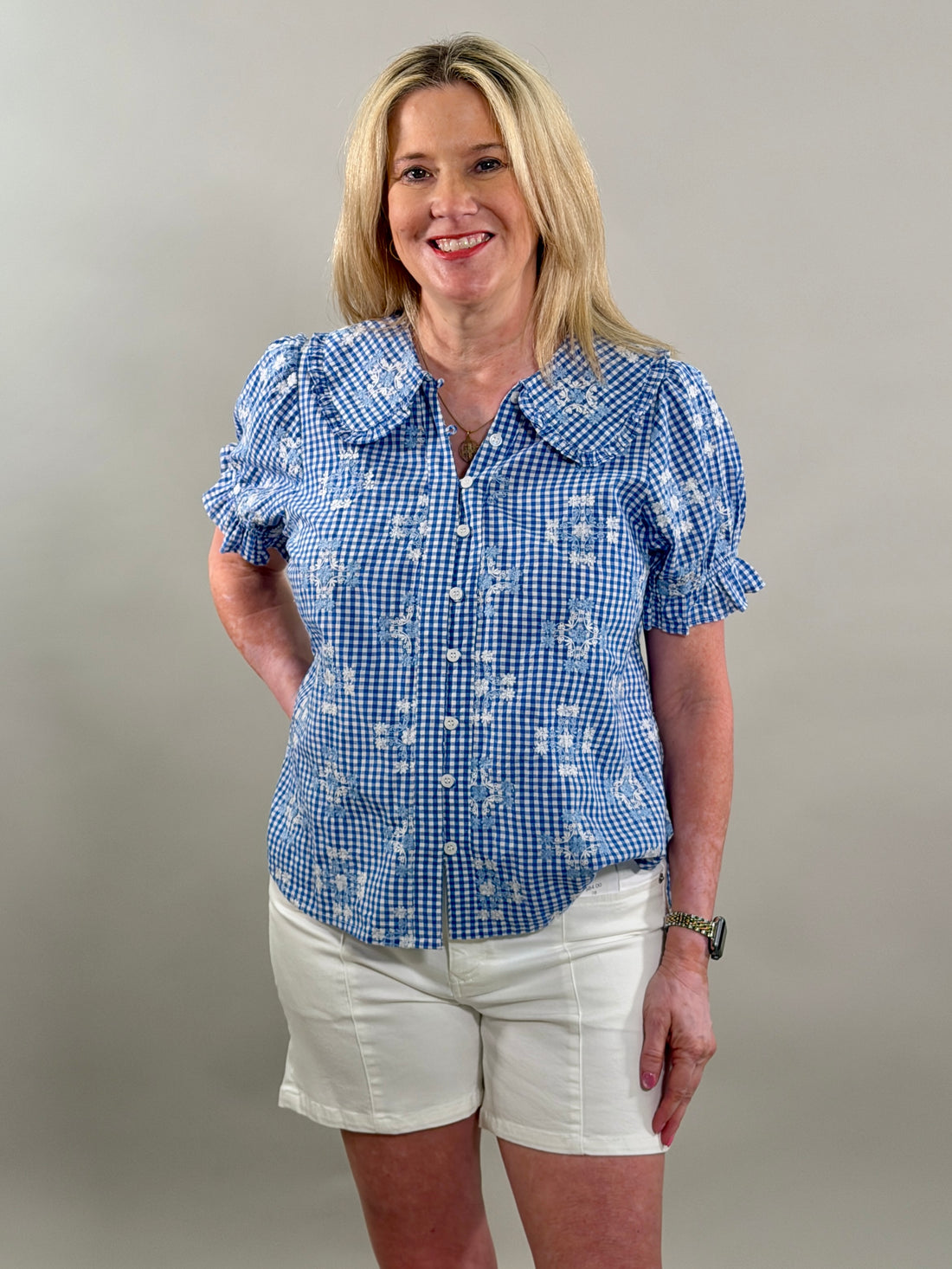 Woman wearing a blue checkered blouse and white shorts against a plain background