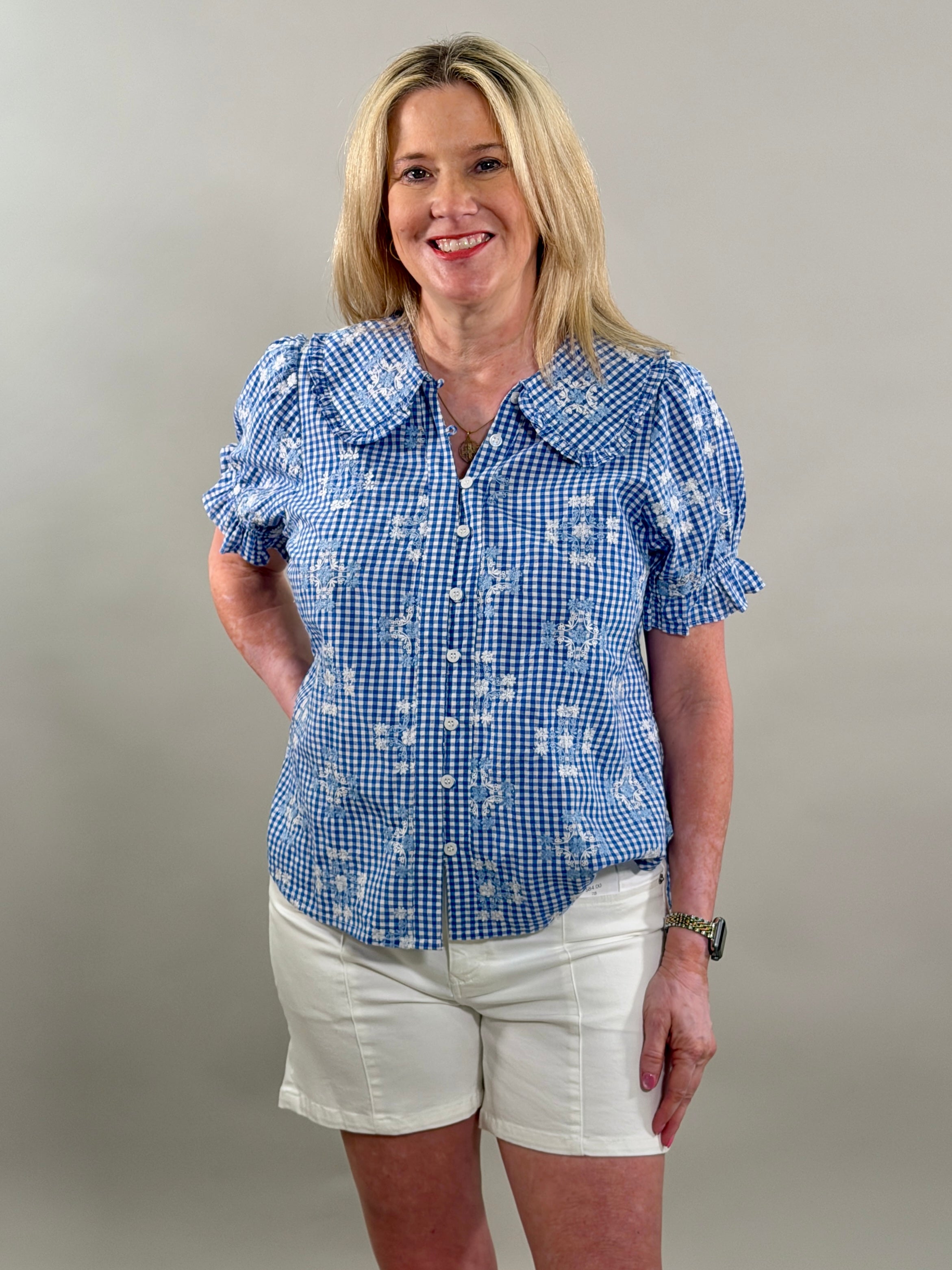 Woman wearing a blue checkered blouse and white shorts against a plain background