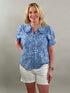 Woman wearing a blue checkered blouse and white shorts against a plain background