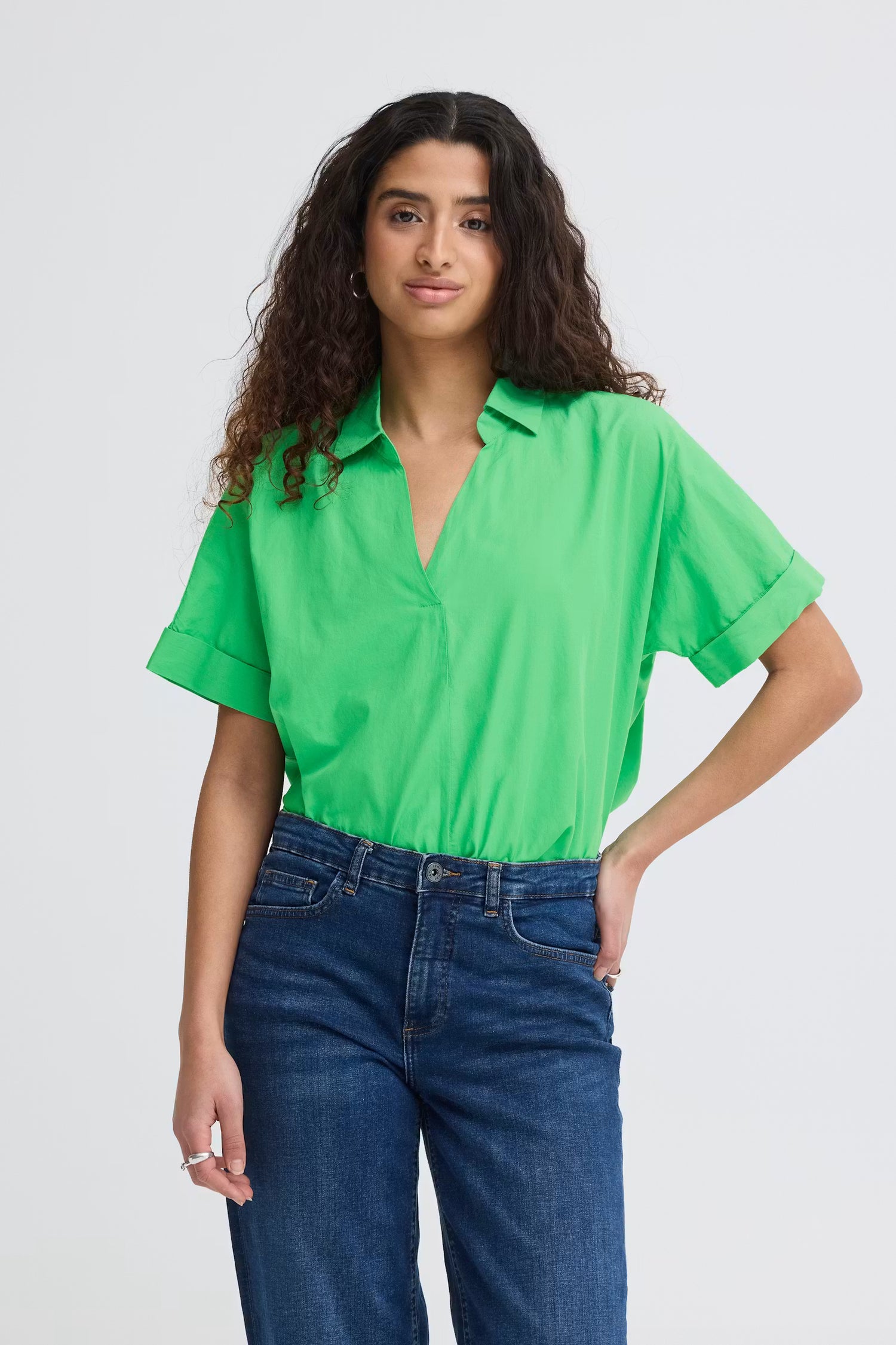 Woman wearing a bright green shirt tucked into blue jeans on a white background