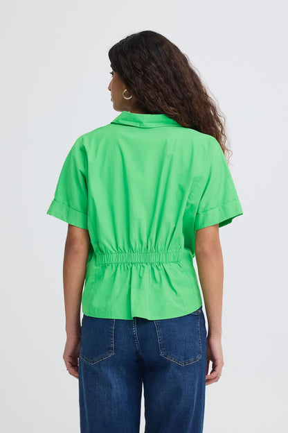 Rear view of a woman wearing a bright green, boxy short sleeve cotton shirt with cinched back with dark wash jeans.