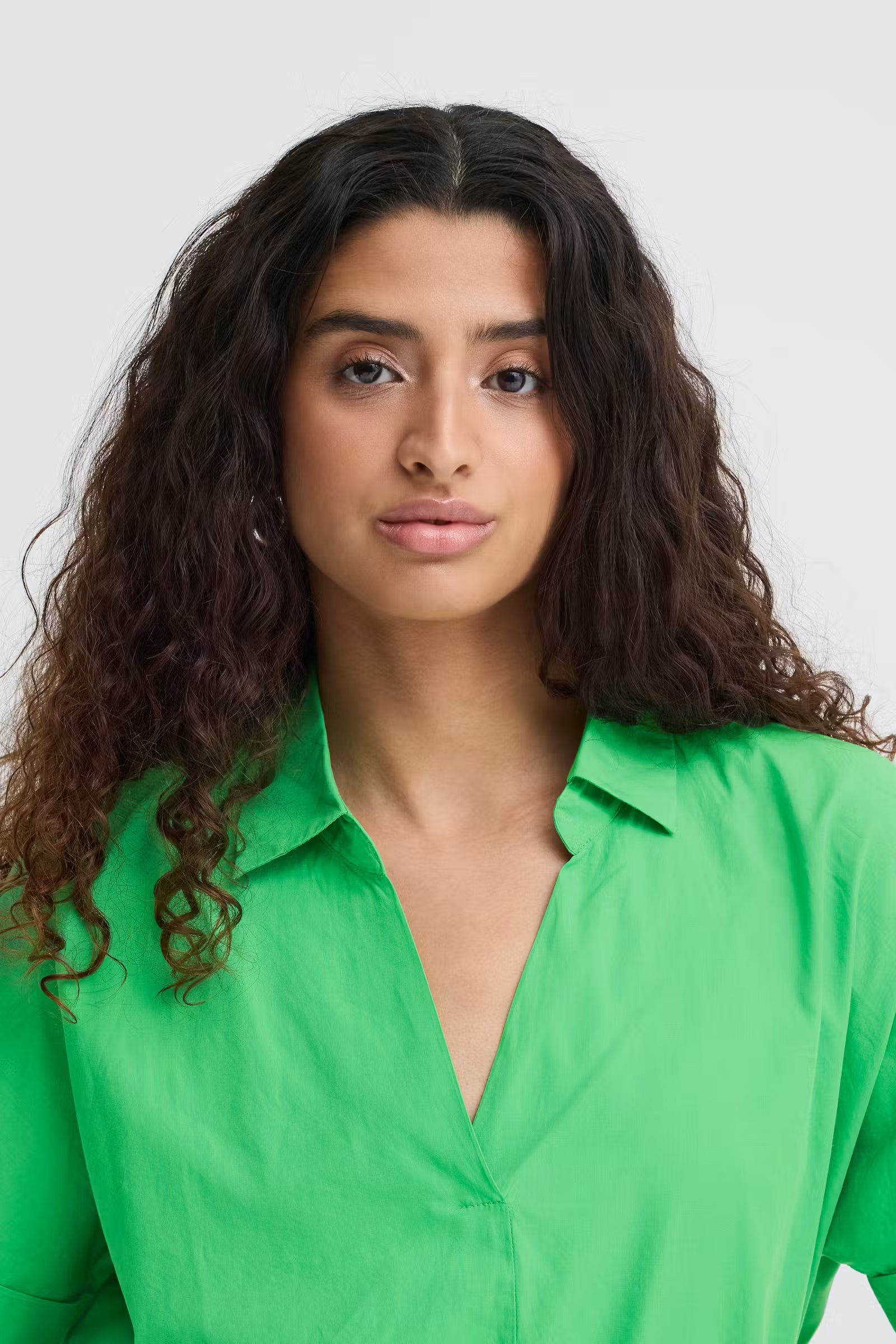 Up close view of a woman wearing a bright green, boxy short sleeve cotton shirt with an open collar and V-neck.