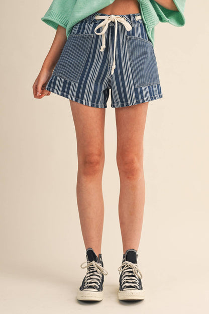 Person wearing blue striped shorts and black sneakers on a beige background