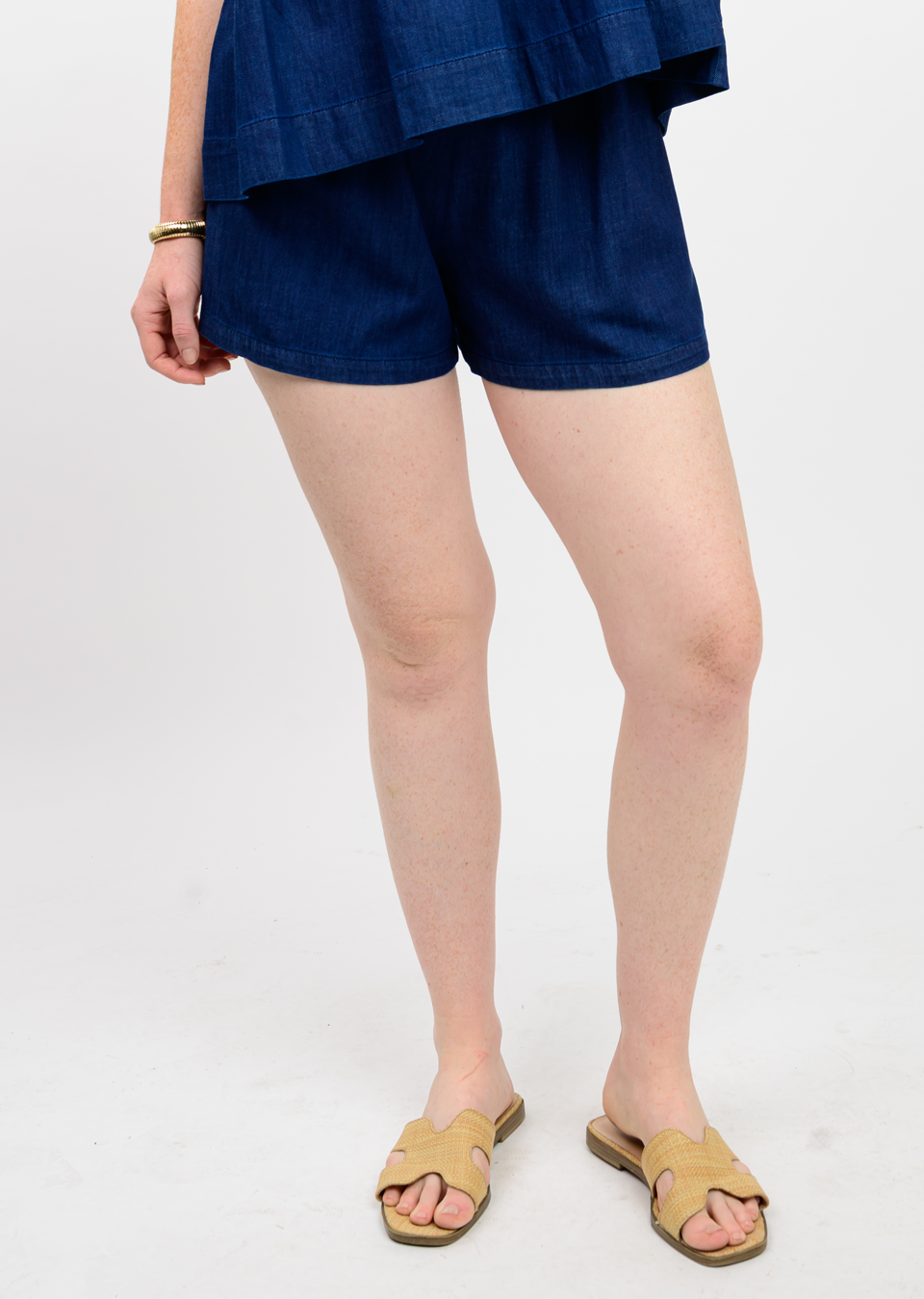Woman wearing dark blue cotton shorts with a smocked waistband and woven slide sandals.