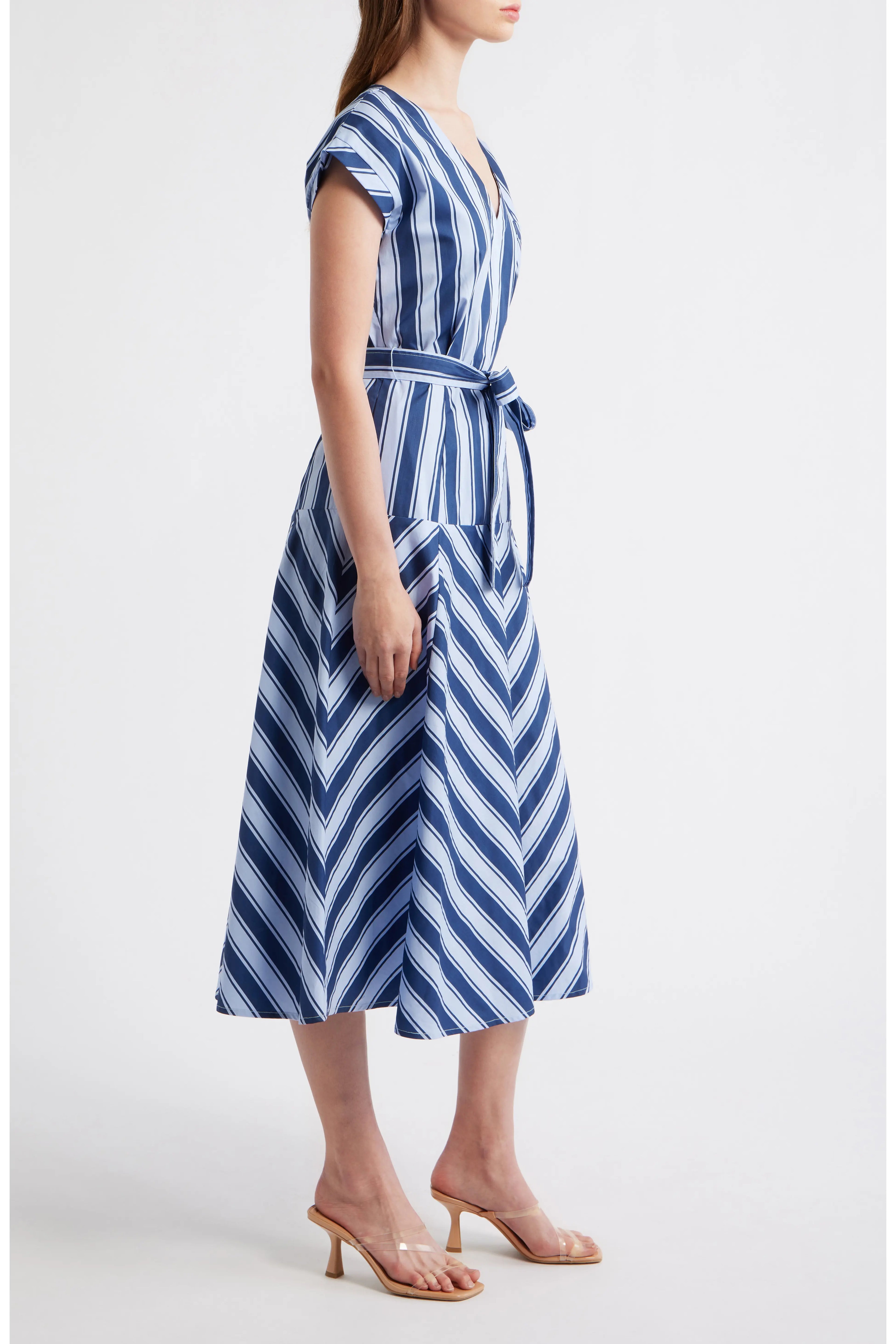 Side view of a woman wearing a blue and white multi-directional striped midi dress with a V-neckline, short cap sleeves, and a matching fabric tie belt.