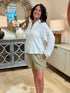 Woman with dark wavy hair wearing a white long-sleeve cotton gauze snap-front shirt with olive green shorts.