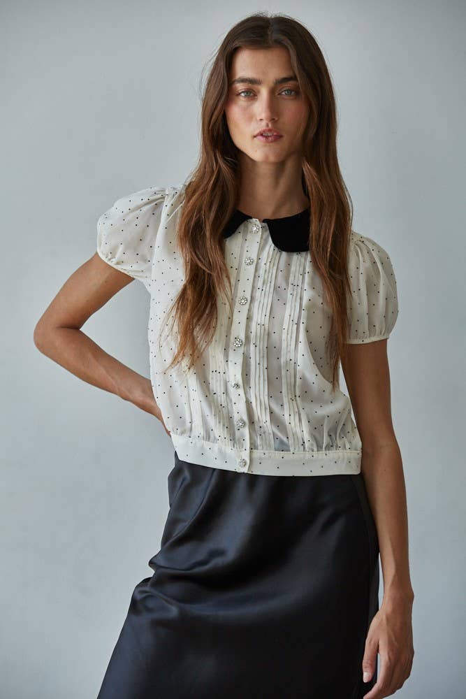 Woman wearing the black and white polka dot blouse with a velvet Peter Pan collar and a black satin skirt.