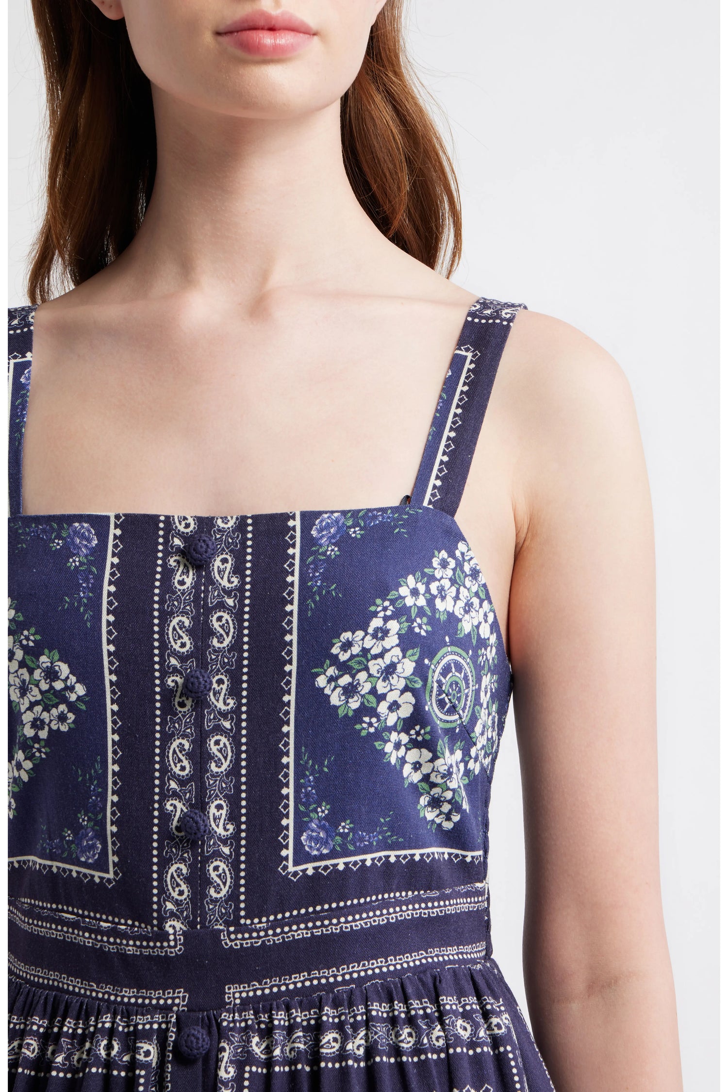 Close up of a woman wearing a navy blue bandana-patterned cotton-linen midi dress with a square neckline, adjustable straps, and a button-front skirt.