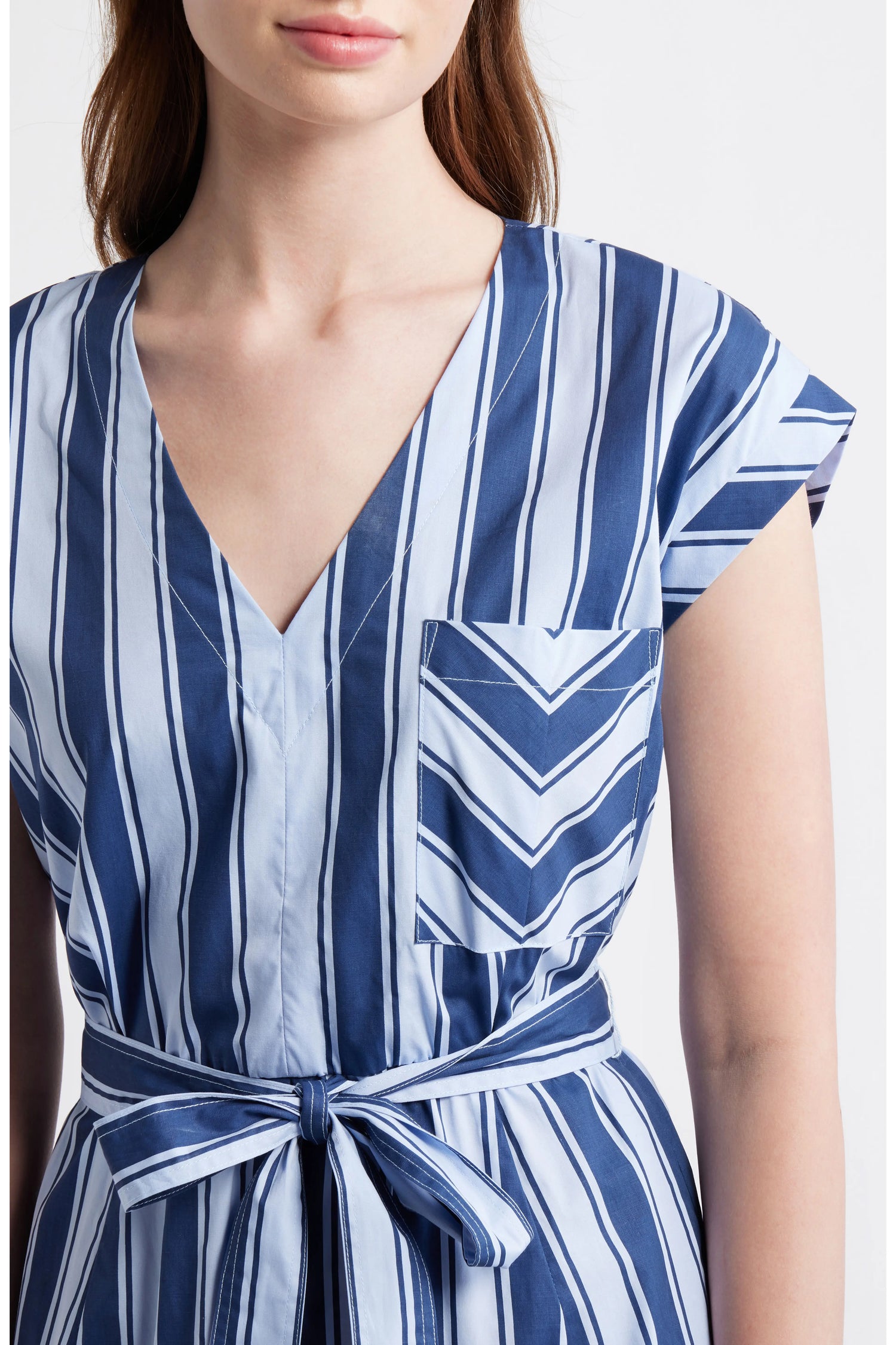 Close up of a woman wearing a blue and white multi-directional striped midi dress with a V-neckline, short cap sleeves, and a matching fabric tie belt.