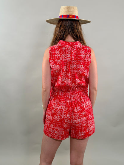 Rear view of a woman wearing a red patterned romper and straw hat on a plain background
