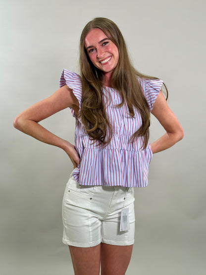 A smiling woman wearing a blue, red, and white striped top and white shorts against a plain background