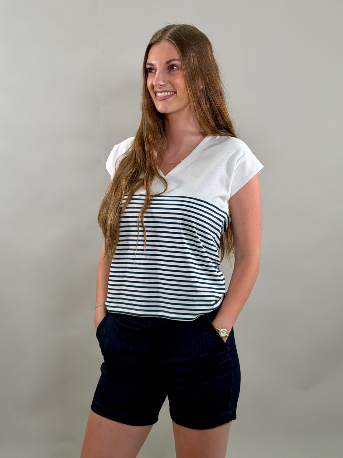 Woman wearing a white and navy striped shirt with navy shorts against a plain background