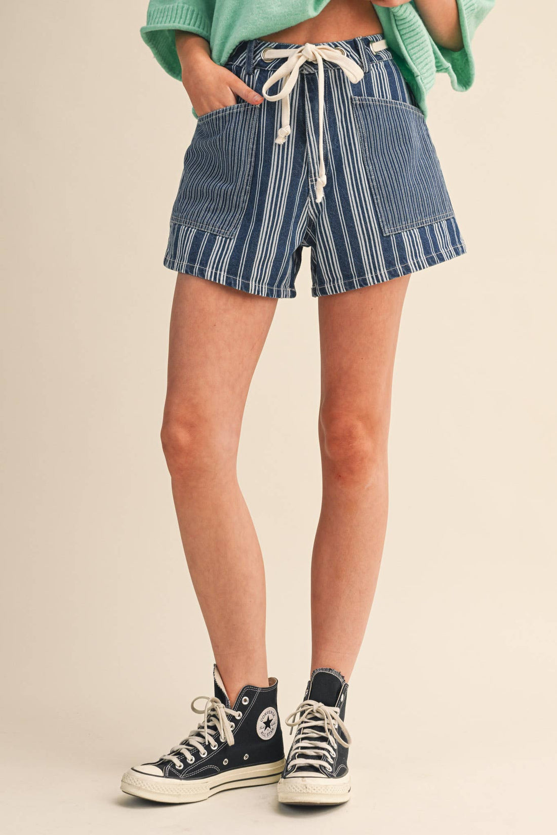 Person wearing blue striped shorts and black Converse sneakers on a beige background