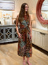 Woman wearing a sleeveless earth-tone botanical print midi dress with a twist front waist.