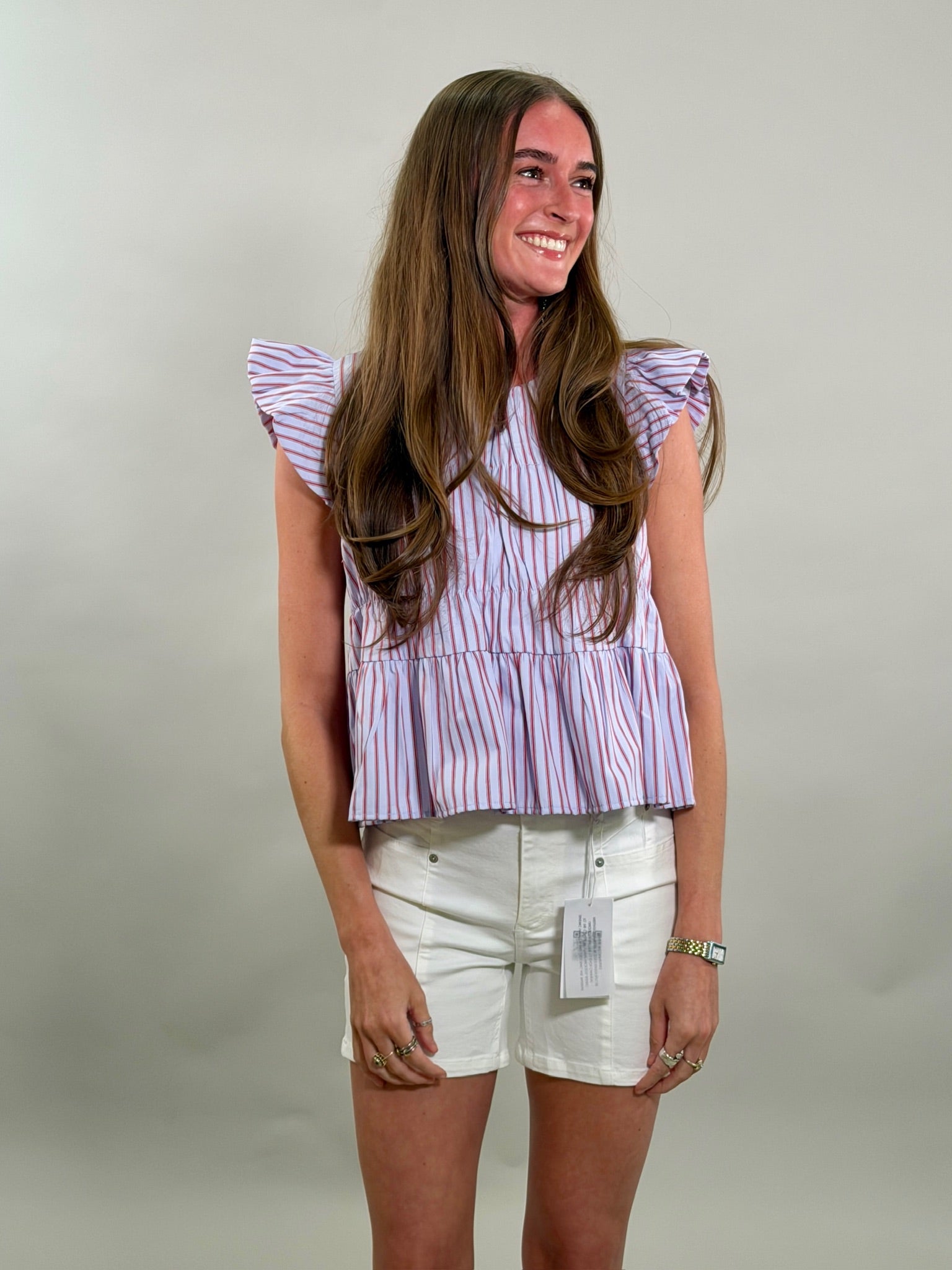 A smiling woman wearing a striped top and white shorts against a plain background