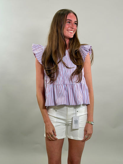 A smiling woman wearing a striped top and white shorts against a plain background