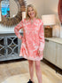 Blonde woman smiling while wearing a pink 100% cotton shift dress with an elaborate coral-colored bohemian placement print down the front.