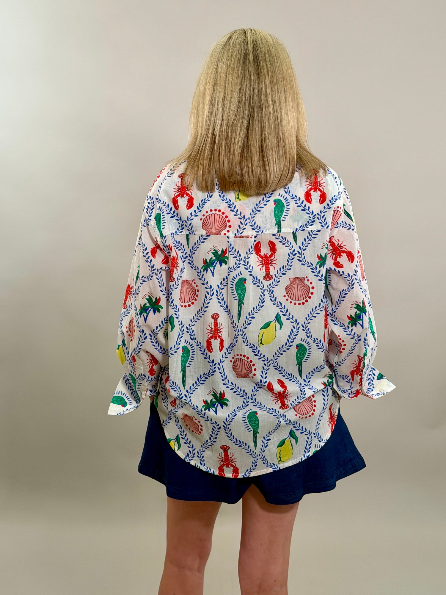 Woman wearing an oversized white button-down shirt with a vibrant blue, red, and yellow coastal print paired with navy shorts.