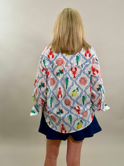 Woman wearing an oversized white button-down shirt with a vibrant blue, red, and yellow coastal print paired with navy shorts.