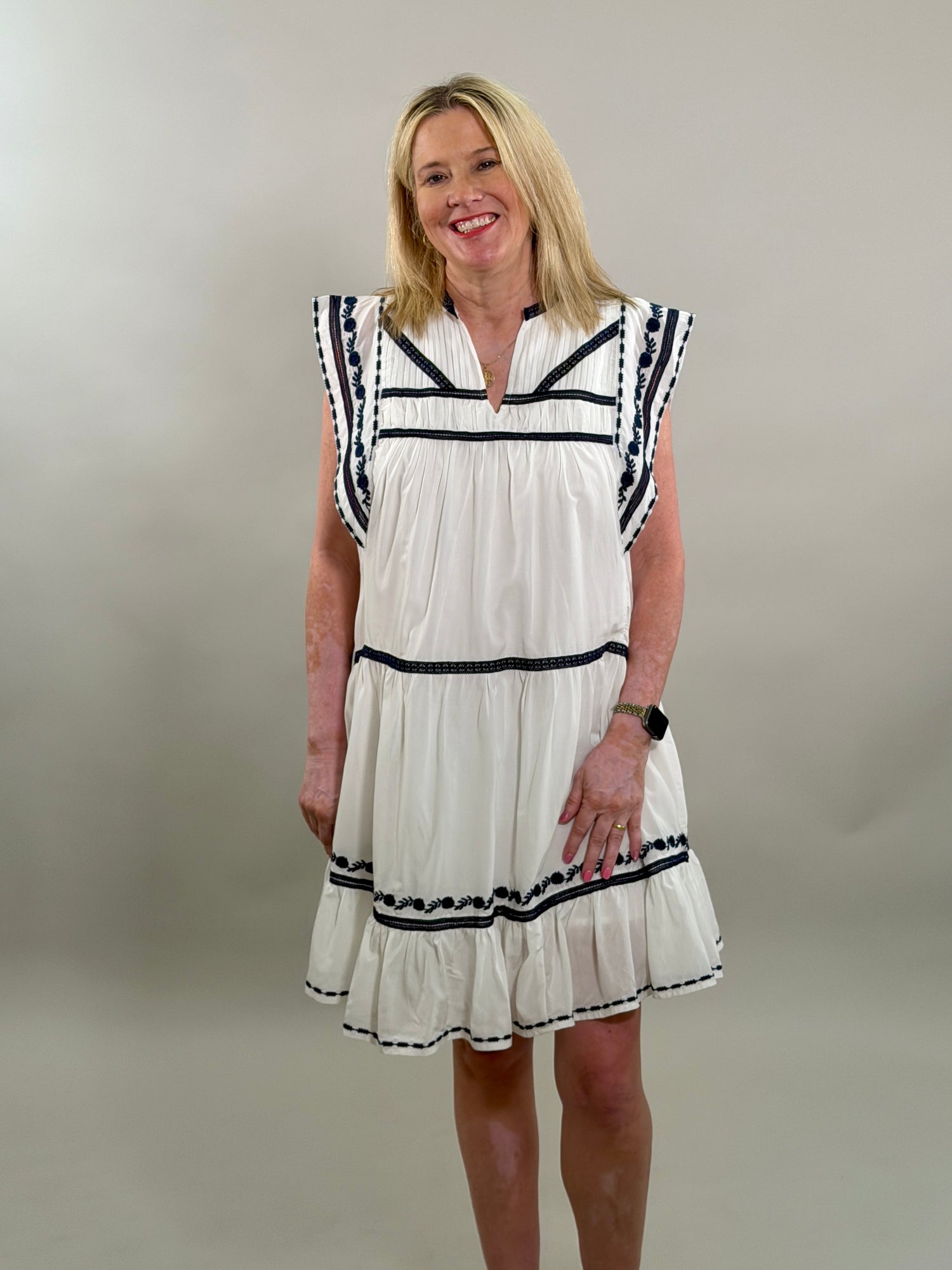 Woman wearing a white dress with navy trim against a plain background