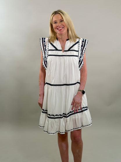 Woman wearing a white dress with navy trim against a plain background