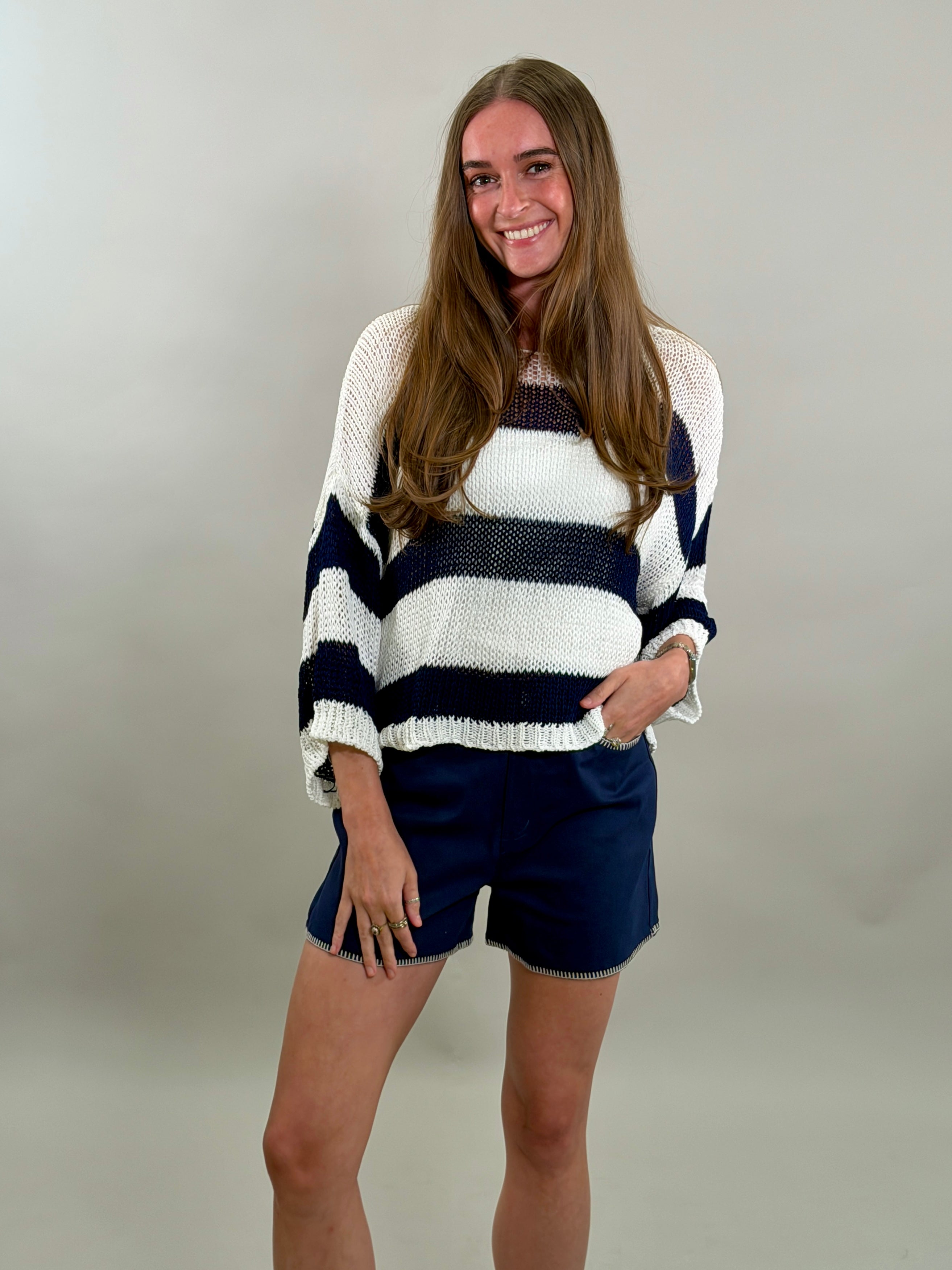 Smiling woman wearing a striped sweater and shorts against a plain background
