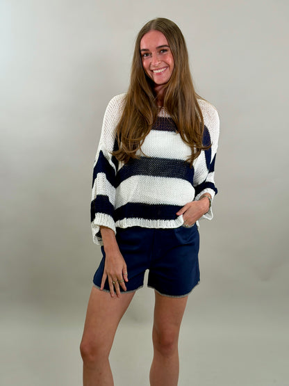 Smiling woman wearing a striped sweater and shorts against a plain background