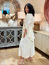 Side full body view of a woman wearing a cream-colored 100% cotton button-down shirt with a tailored pintuck back waist detail with matching cream midi skirt.