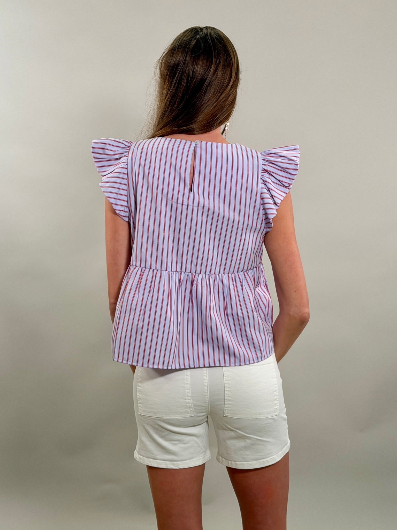 Rear view of a woman wearing a blue, red, and white striped top with ruffled sleeves on a plain background