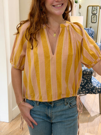 Close up of a smiling young woman taking a mirror selfie wearing a peach and mustard yellow striped cotton blouse with blue jeans.
