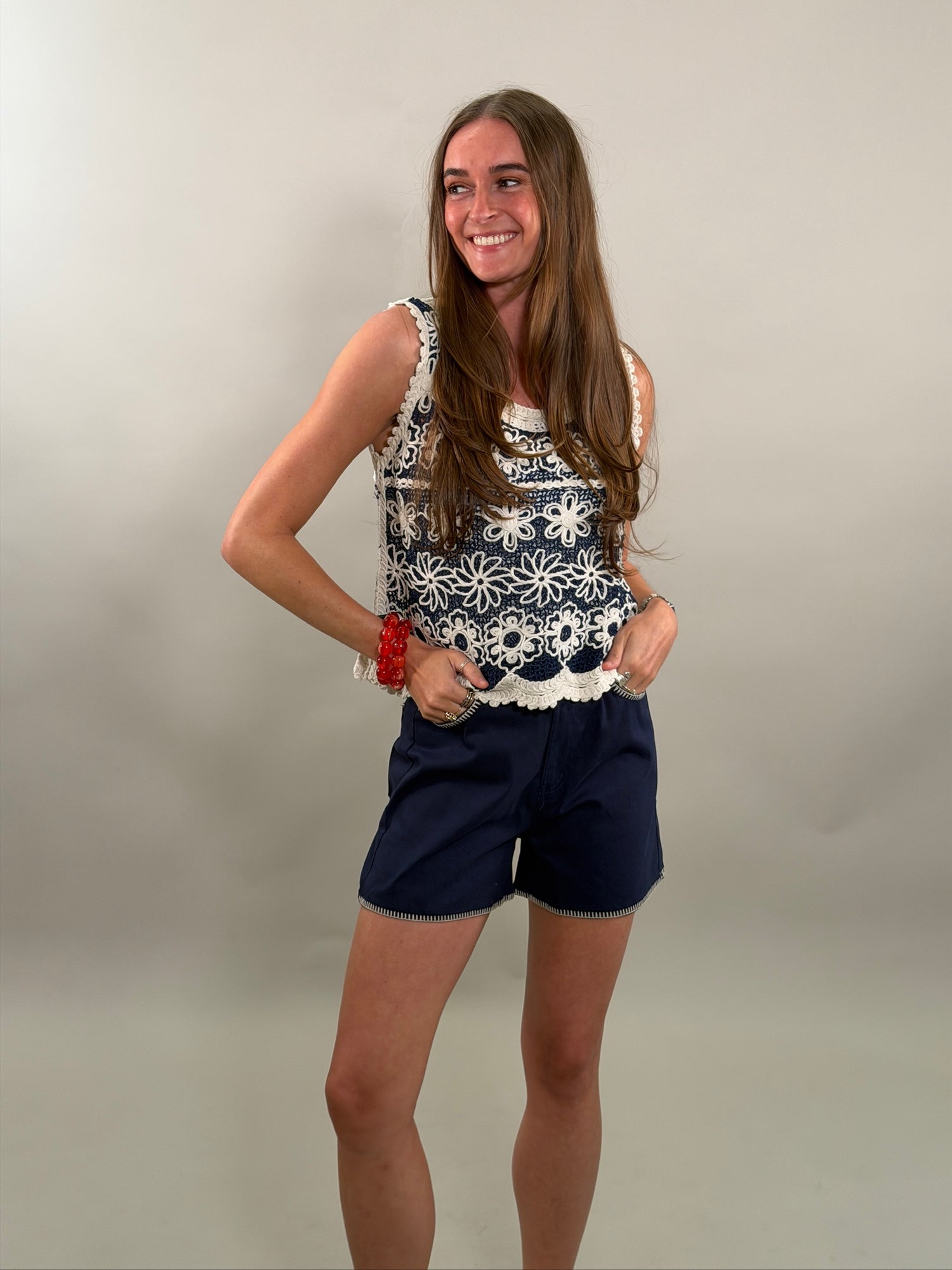 Woman wearing a sleeveless top with white floral pattern and navy shorts on a plain background