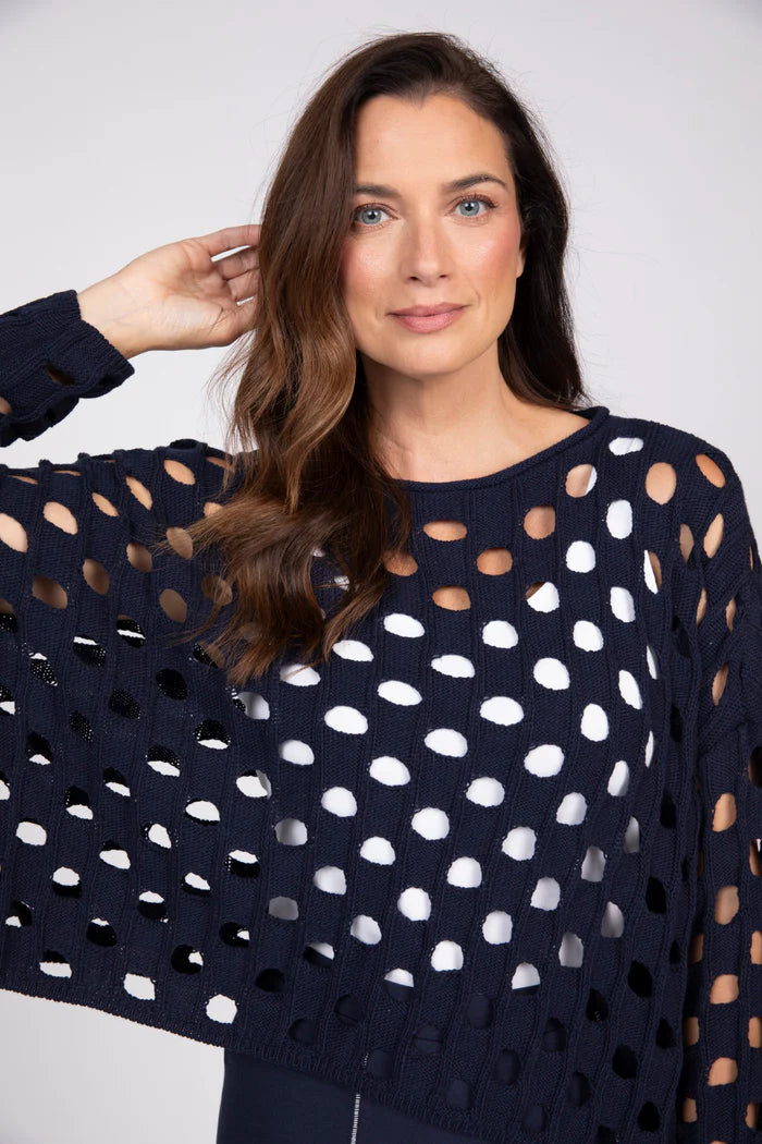 Close up view of a woman wearing a navy blue open-knit cotton sweater over a white tank top.