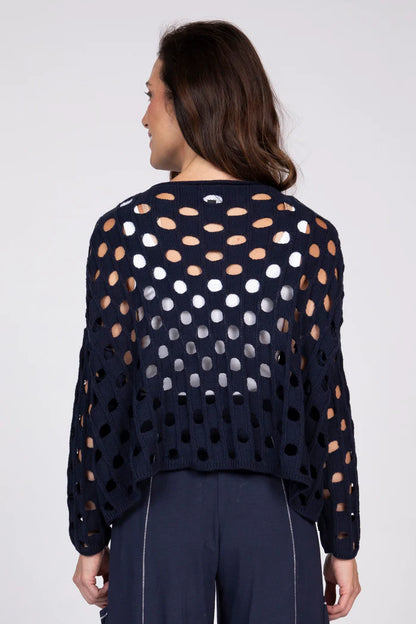 Rear view of a woman wearing a navy blue open-knit cotton sweater over a white tank top.