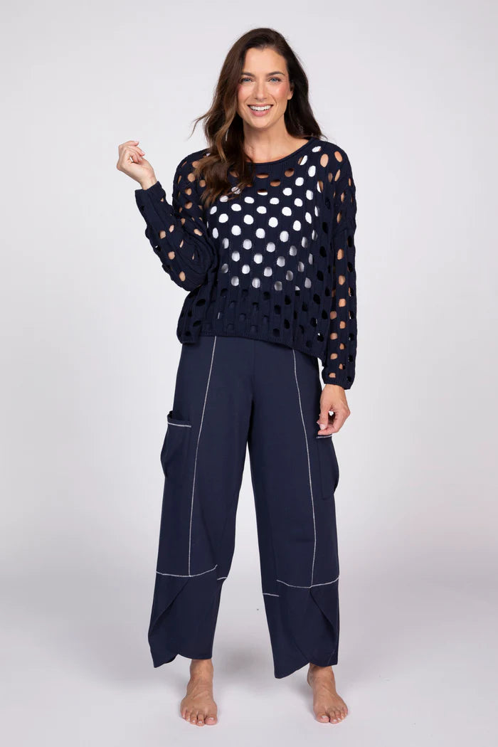 Full body view of a woman wearing a navy blue open-knit cotton sweater over a white tank top with navy pants.